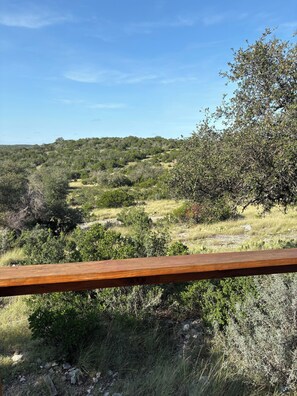 Une vue depuis un balcon en bois donnant sur un paysage vallonné, caractérisé par une végétation luxuriante et un ciel dégagé.