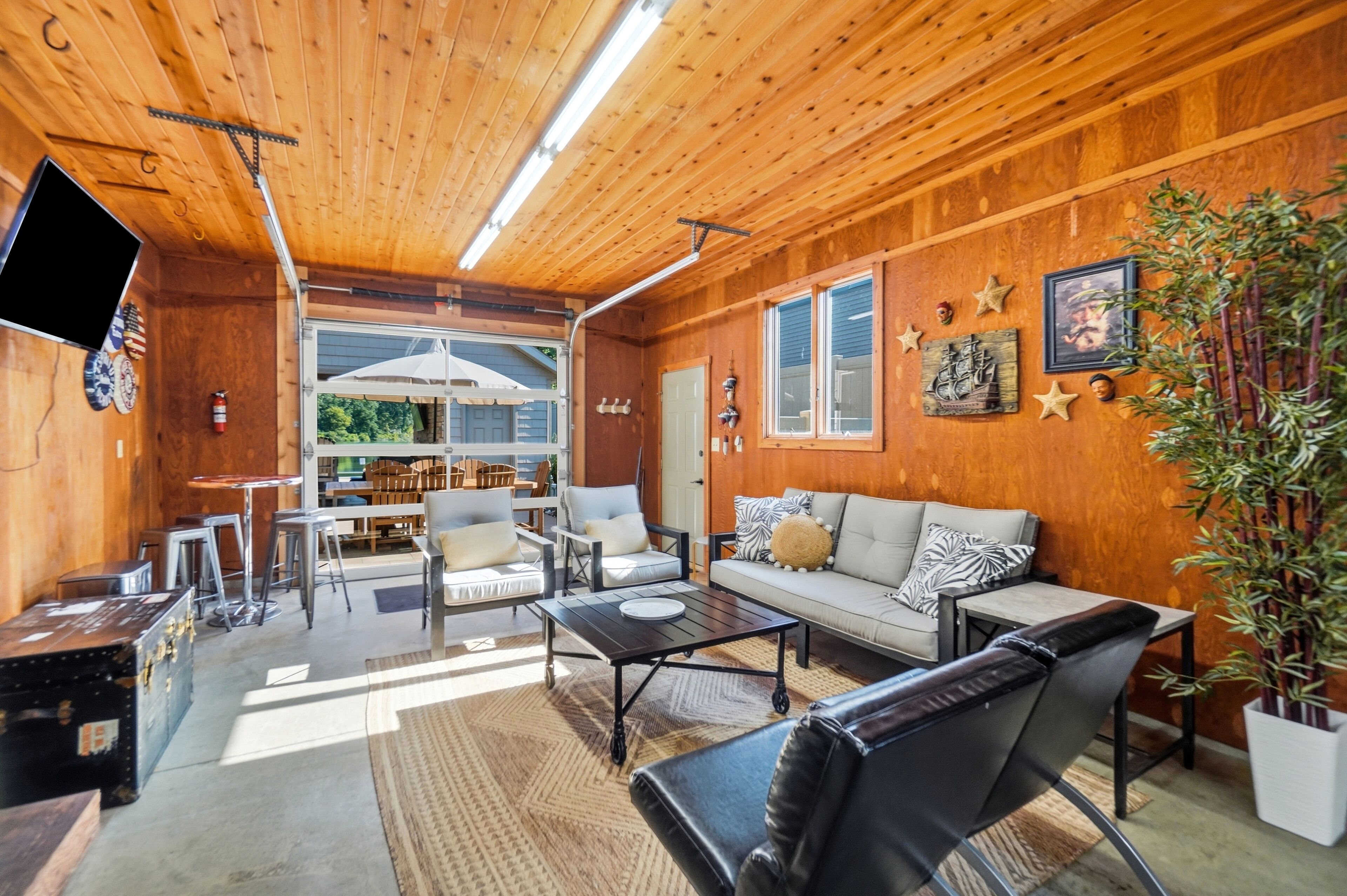 L’intérieur chaleureux d’un chalet avec un plafond en bois, un ensemble de canapés, un coin repas et un téléviseur fixé au mur.