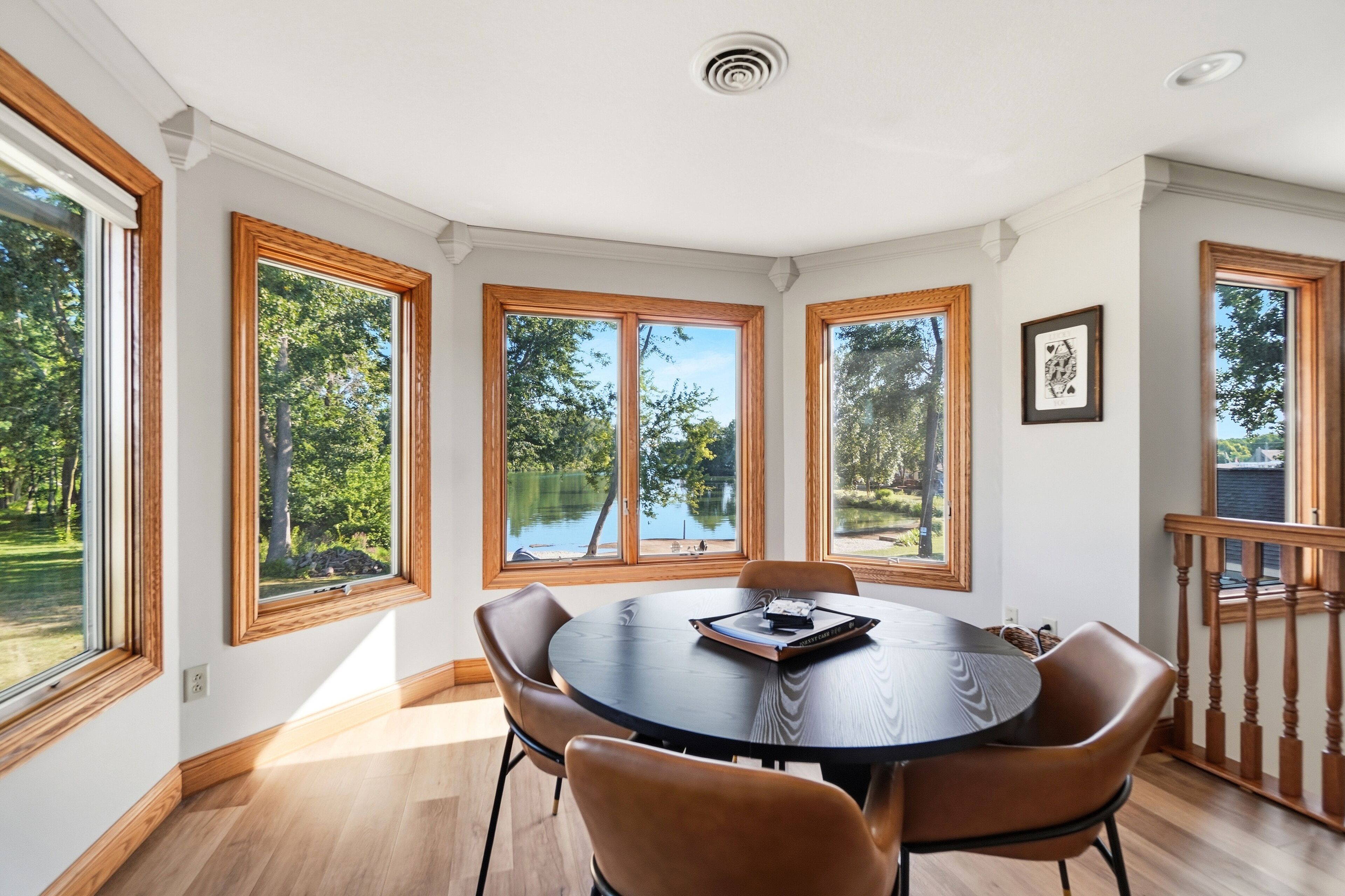 Un coin repas comprenant une table ronde, quatre chaises et de grandes fenêtres donnant sur un lac et des arbres.
