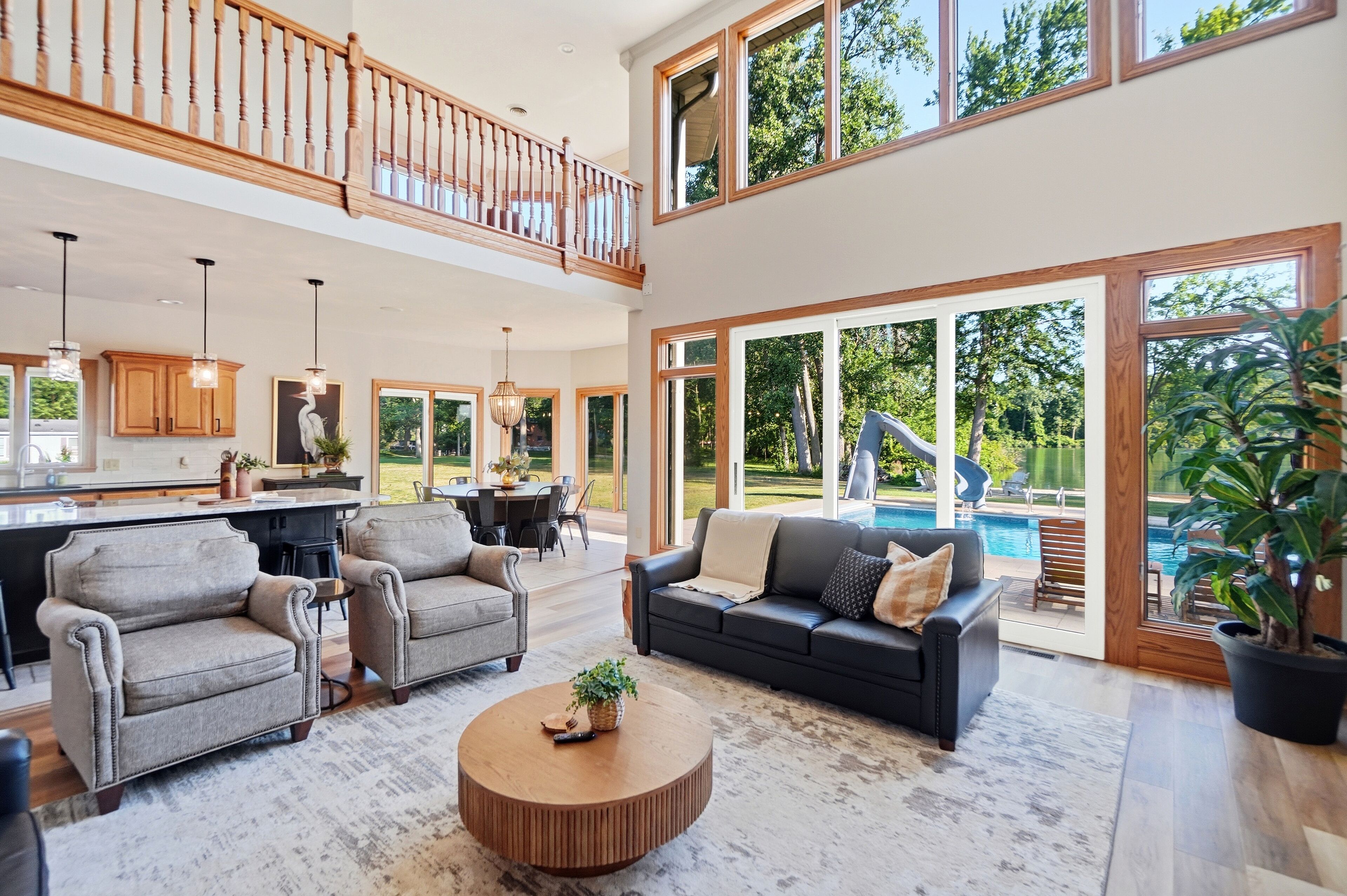 A spacious living area with a high ceiling, a dining area, and a view of a swimming pool.