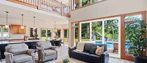 A spacious living area with a high ceiling, a dining area, and a view of a swimming pool.