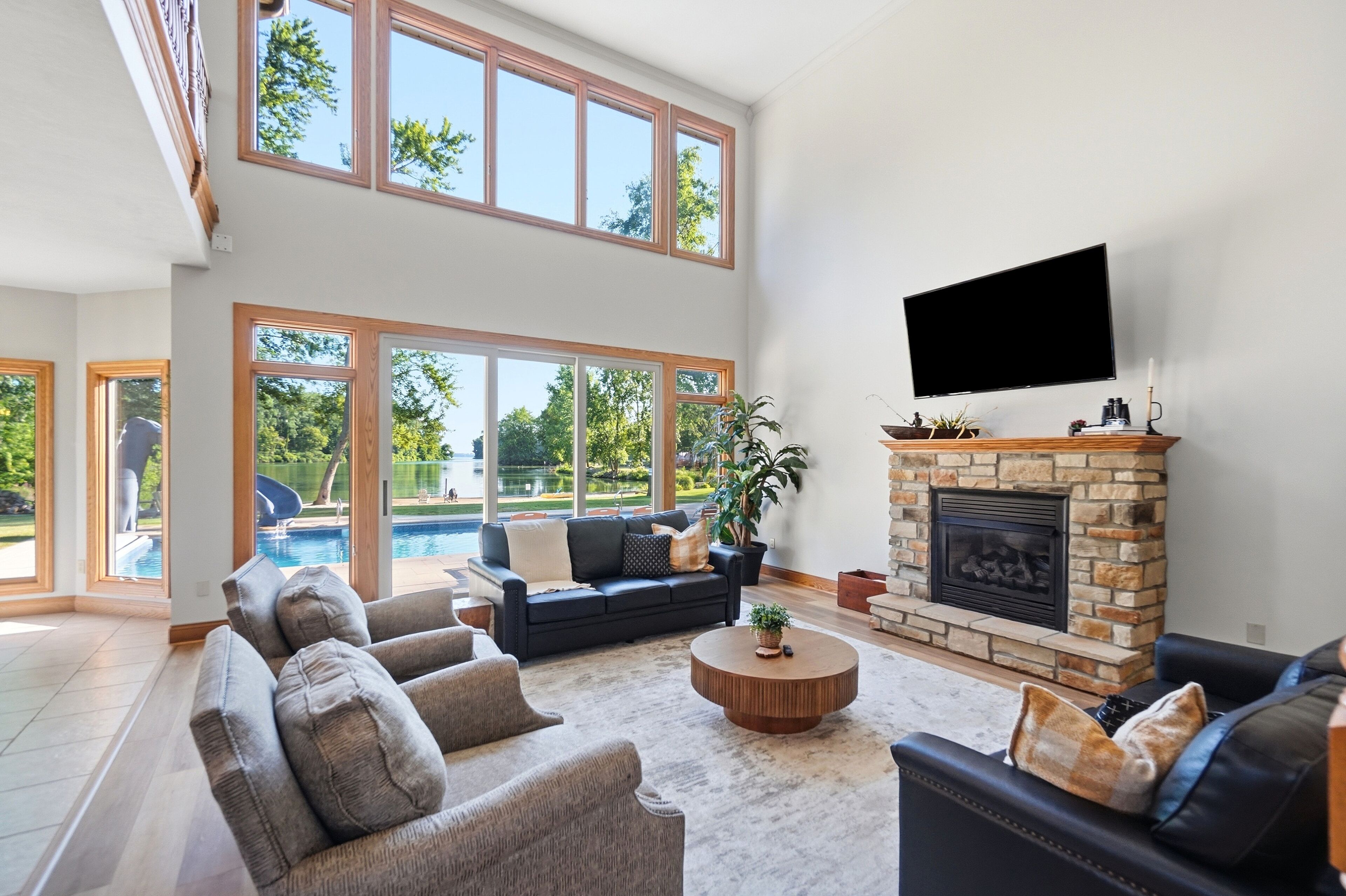 A spacious living room with a fireplace, a large flat-screen TV, and a view of a swimming pool.