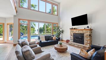 A spacious living room with a fireplace, a large flat-screen TV, and a view of a swimming pool.