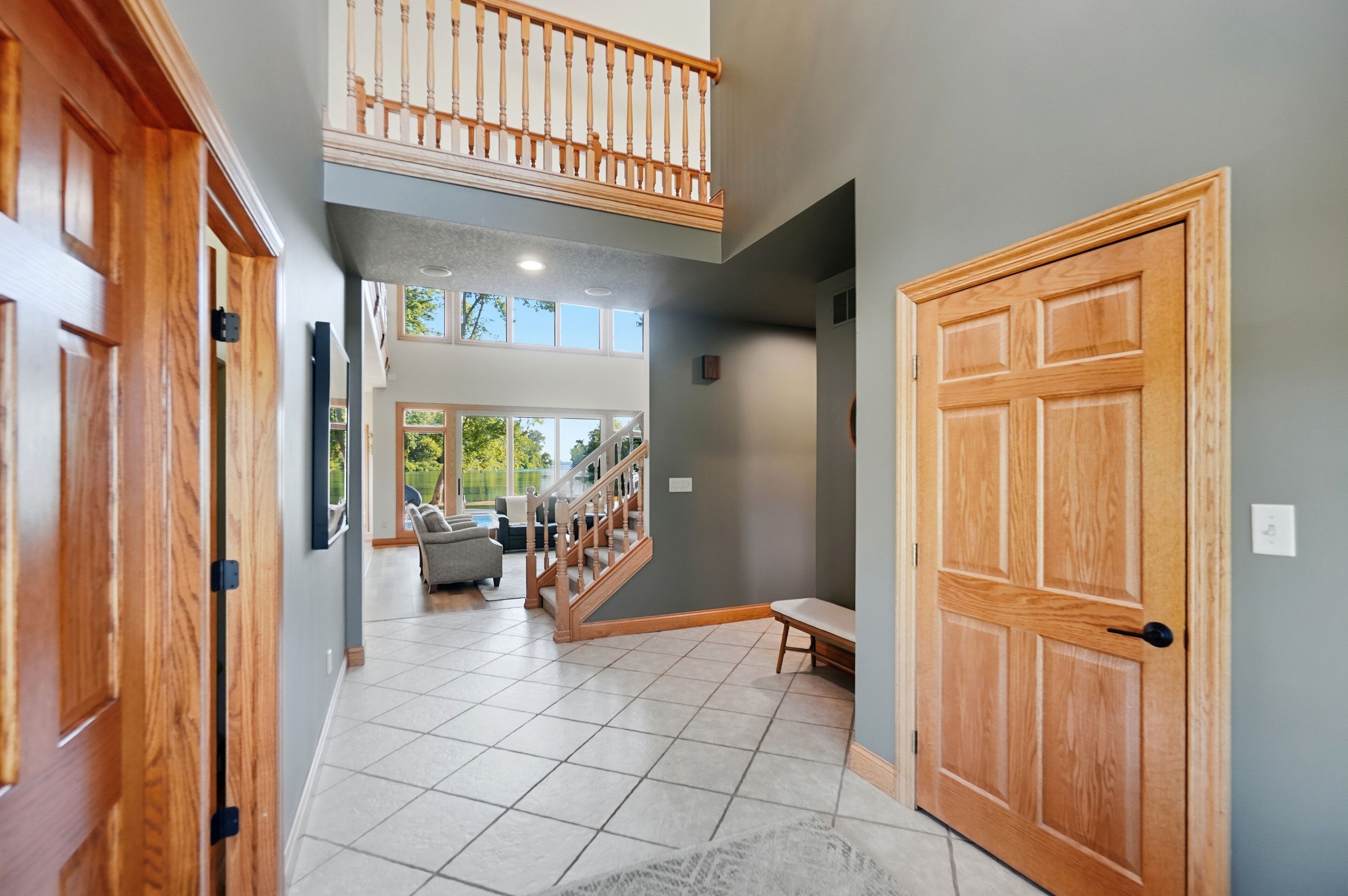 A spacious hallway with a wooden staircase leading to a second floor, a large wooden door, and a view of a living area with a sofa and a dining table.
