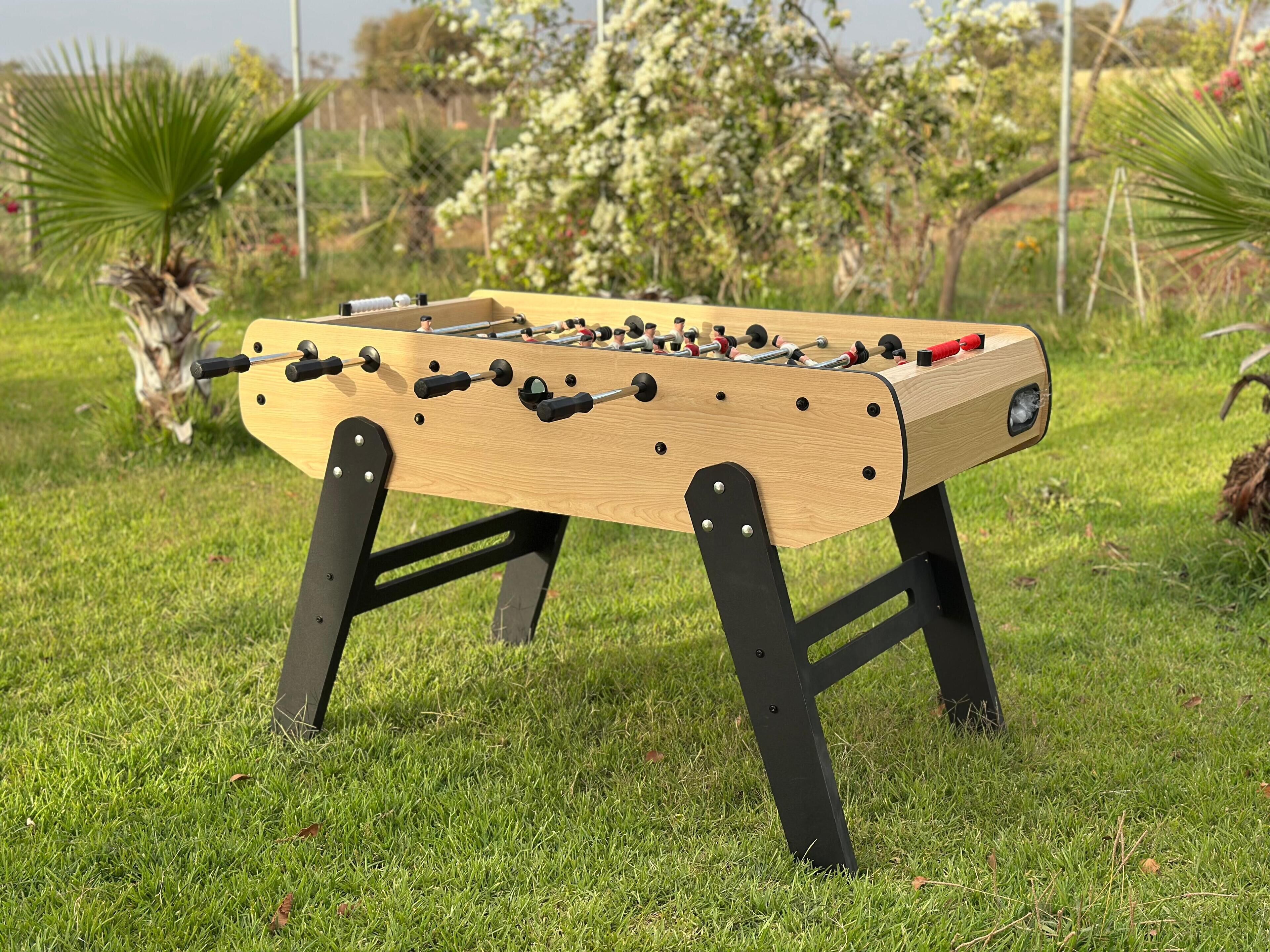 Una mesa de fútbol de madera con patas negras, sobre un césped.