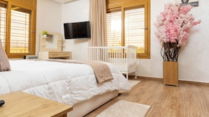 Een slaapkamer met een groot bed, een ledikant, een televisie en een decoratieve plant.