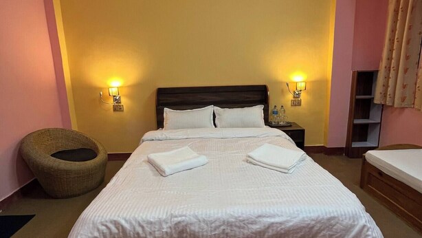 A neatly made bed with white linens, two wall-mounted lamps, and a wicker chair. - Peaceful, Charming- bedroom bed & breakfast in lovely Dhulikhel #5 (Dhulikhel)