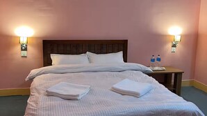 A neatly made bed with white linens and folded towels, two wall-mounted lamps, and a small bedside table with water bottles. - Peaceful, Charming- bedroom bed & breakfast in lovely Dhulikhel #6 (Dhulikhel)