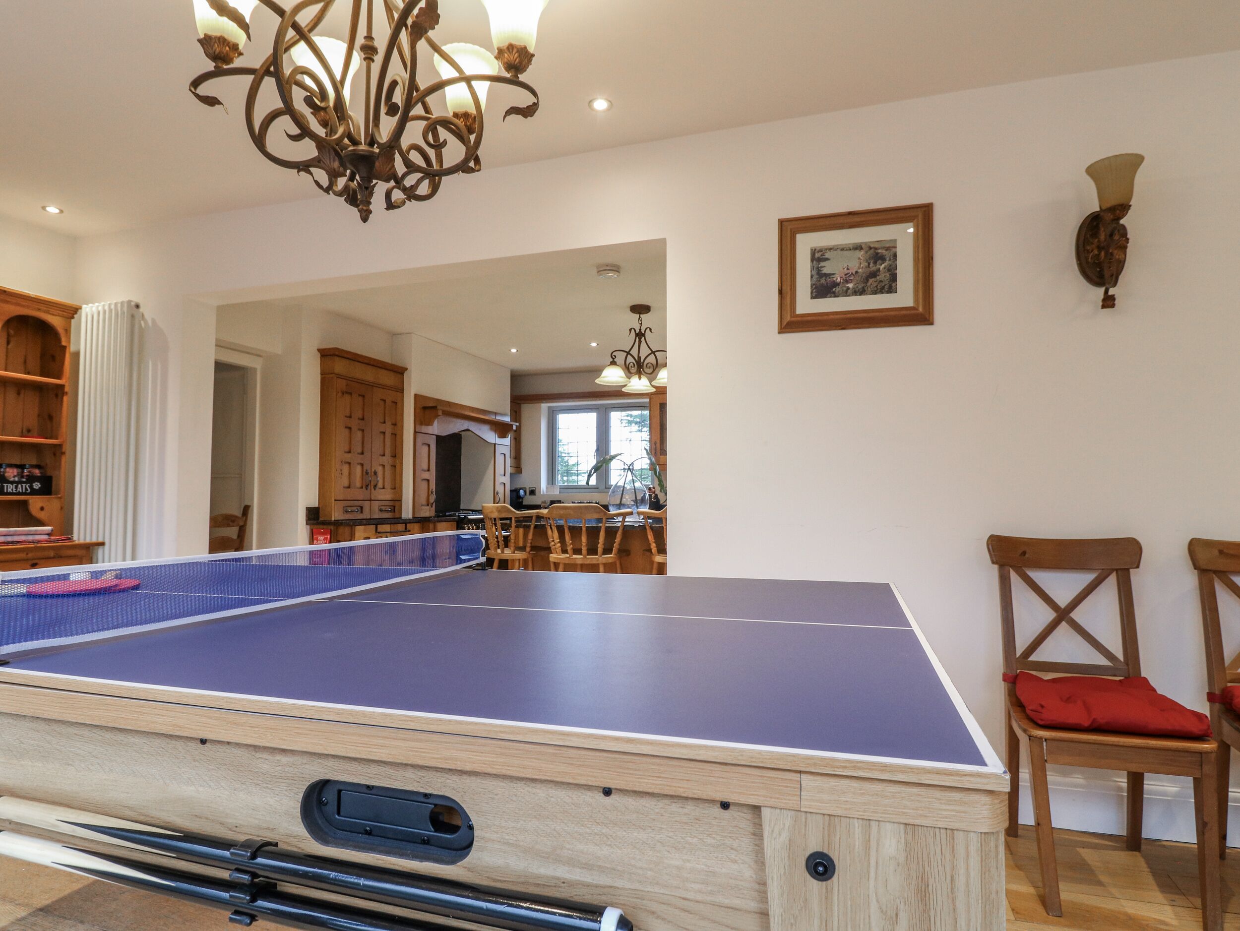 A ping pong table in a room with wooden cabinets, a chandelier, and a framed picture on the wall.