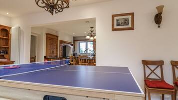 A ping pong table in a room with wooden cabinets, a chandelier, and a framed picture on the wall.
