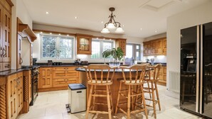 Une cuisine moderne avec des meubles en bois, un îlot central doté de chaises, un réfrigérateur et une fenêtre laissant entrer la lumière naturelle.
