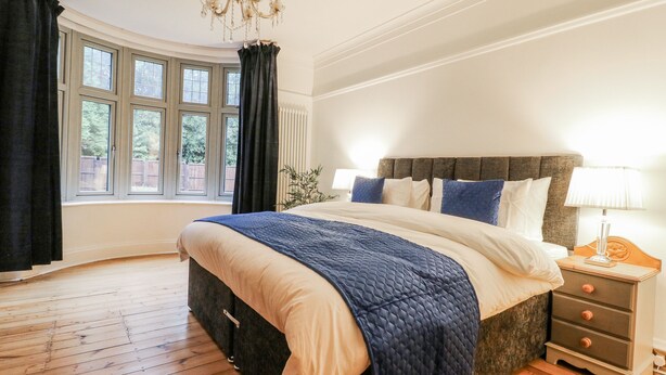 Une chambre à coucher avec un grand lit, une table de chevet, une lampe, un lustre et une fenêtre avec des rideaux.