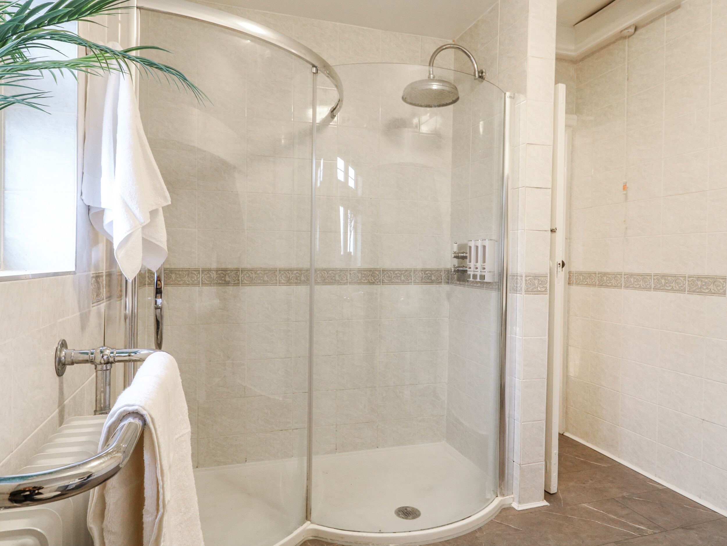A glass-enclosed shower with a handheld showerhead, a glass door, and a white towel hanging on a metal towel rack.