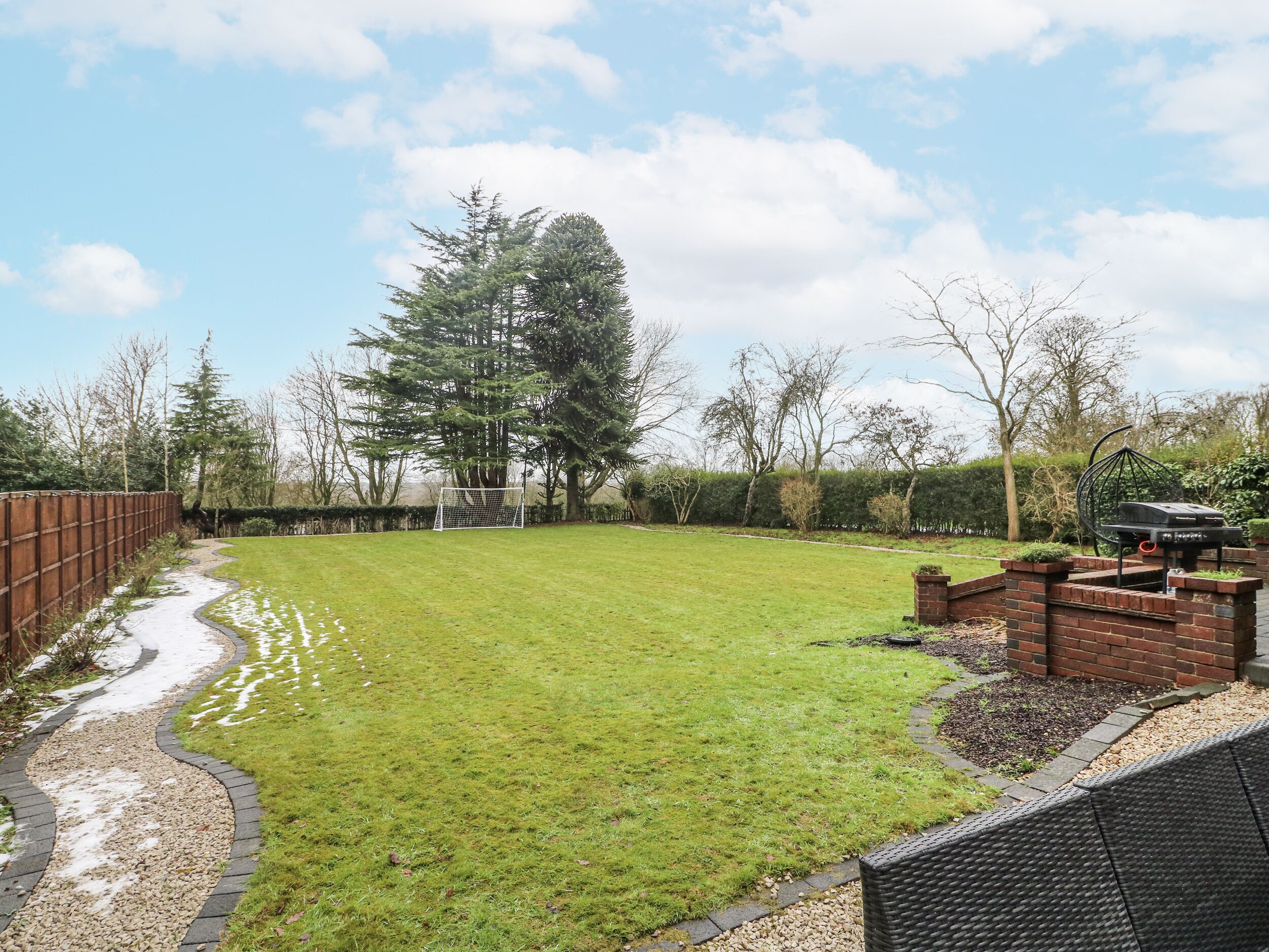A backyard with a grassy lawn, a brick patio, and a large tree.