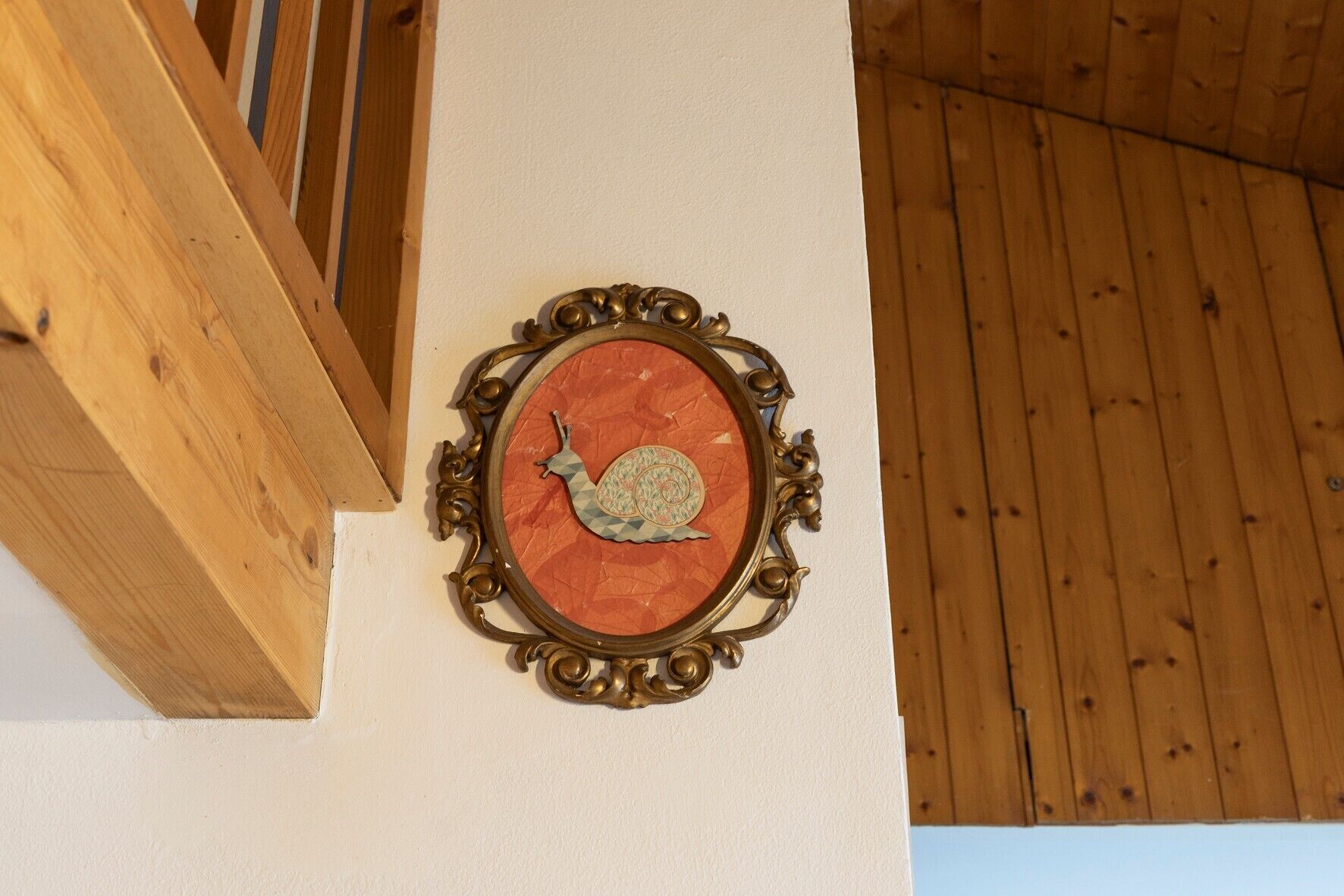 Una pieza decorativa montada en la pared con diseño de caracol, techo de madera y pared blanca.