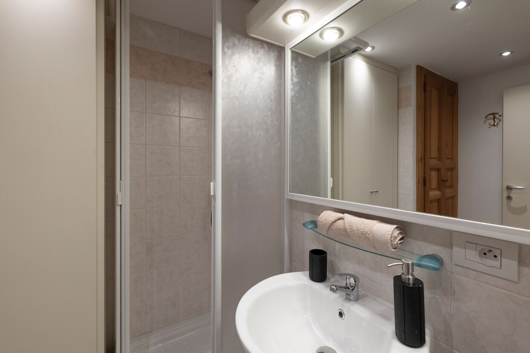 Moderni kylpyhuone, jossa on lasinen suihkuseinä, valkoinen pesuallas, peili ja pyyhekoukku.