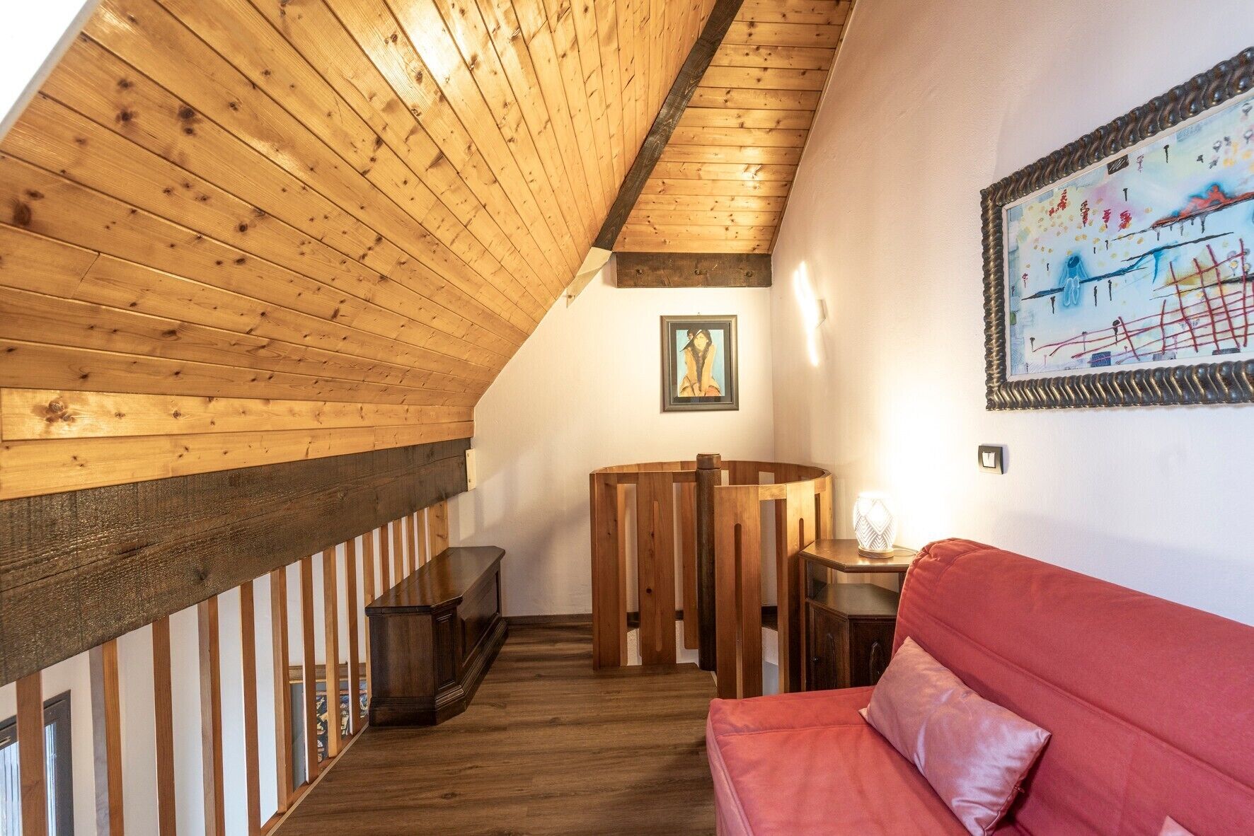 Acogedor dormitorio en el ático con vigas de madera, un sofá rojo, una mesita y un cuadro en la pared.