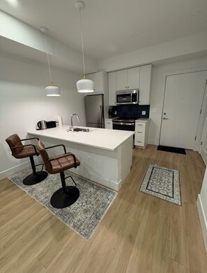 Une cuisine moderne dotée d’un îlot central, d’appareils électroménagers en acier inoxydable et de luminaires suspendus.