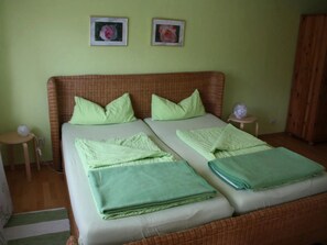 Uma cama de casal com roupa de cama verde, dois travesseiros, um painel de cabeça de vime e duas molduras na parede.