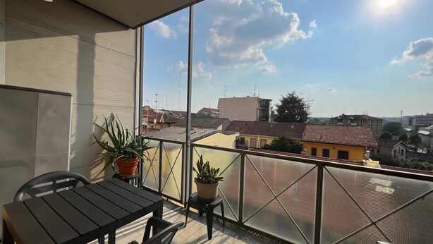 Un balcon avec une table et des chaises, des plantes en pot et une vue sur les bâtiments environnants.
