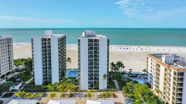 A high-rise hotel with a pool, beach view, and palm trees. - Island Winds 624 Gulf front (Fort Myers Beach)