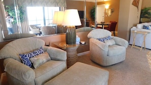 A living room with two armchairs, a coffee table, and a lamp. There is a mirror reflecting the room, a dining area with a table and chairs, and a sofa in the background. - Island Winds 624 Gulf front (Fort Myers Beach)