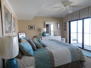 A bedroom with a bed, a ceiling fan, a dresser, a mirror, and a balcony with chairs. - Island Winds 624 Gulf front (Fort Myers Beach)