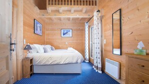 A wooden cabin bedroom with a bed, a nightstand, a mirror, and a radiator. - Simply Morzine - Chalet Central (Morzine)