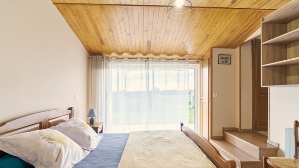 Ein Schlafzimmer mit Holzboden, einem Bett mit weißer und blauer Bettwäsche, einem Stuhl und einem Fenster mit Vorhängen.