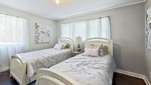 Quarto com duas camas de solteiro, uma mesinha de cabeceira com abajur e uma obra de arte na parede.