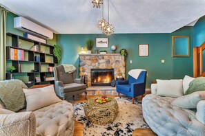 A cozy living room with a stone fireplace, comfortable seating, a bookshelf, and decorative lighting. - The Cozy Owl – 3-Level Cabin Near Arrowhead Lake w/ Fireplace & Firepit (Pocono Lake)