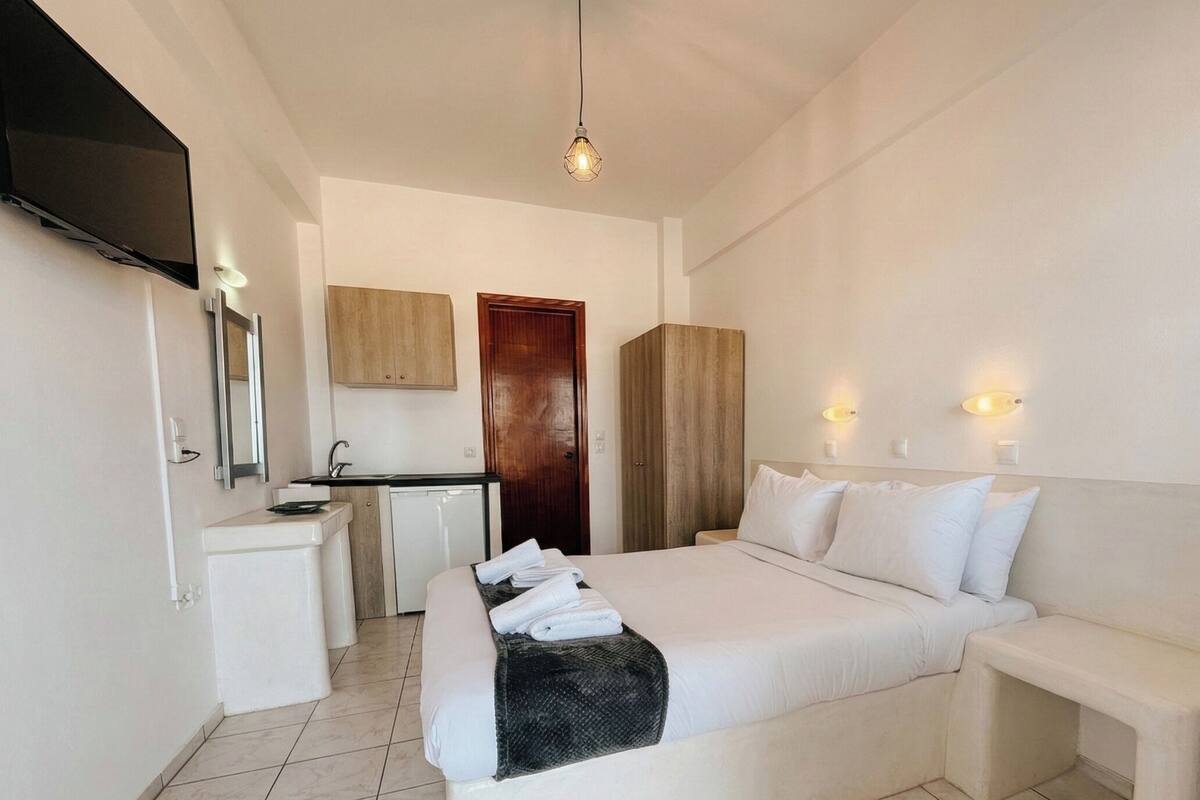 Ein Hotelzimmer mit Bett, Nachttisch, Schreibtisch mit Stuhl, Spiegel, Fernseher und Tür.