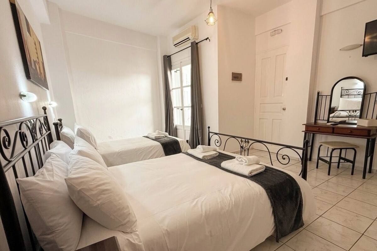Ein Hotelzimmer mit zwei Betten, einem Schreibtisch, einem Stuhl, einem Spiegel und einem Fenster mit Vorhängen.