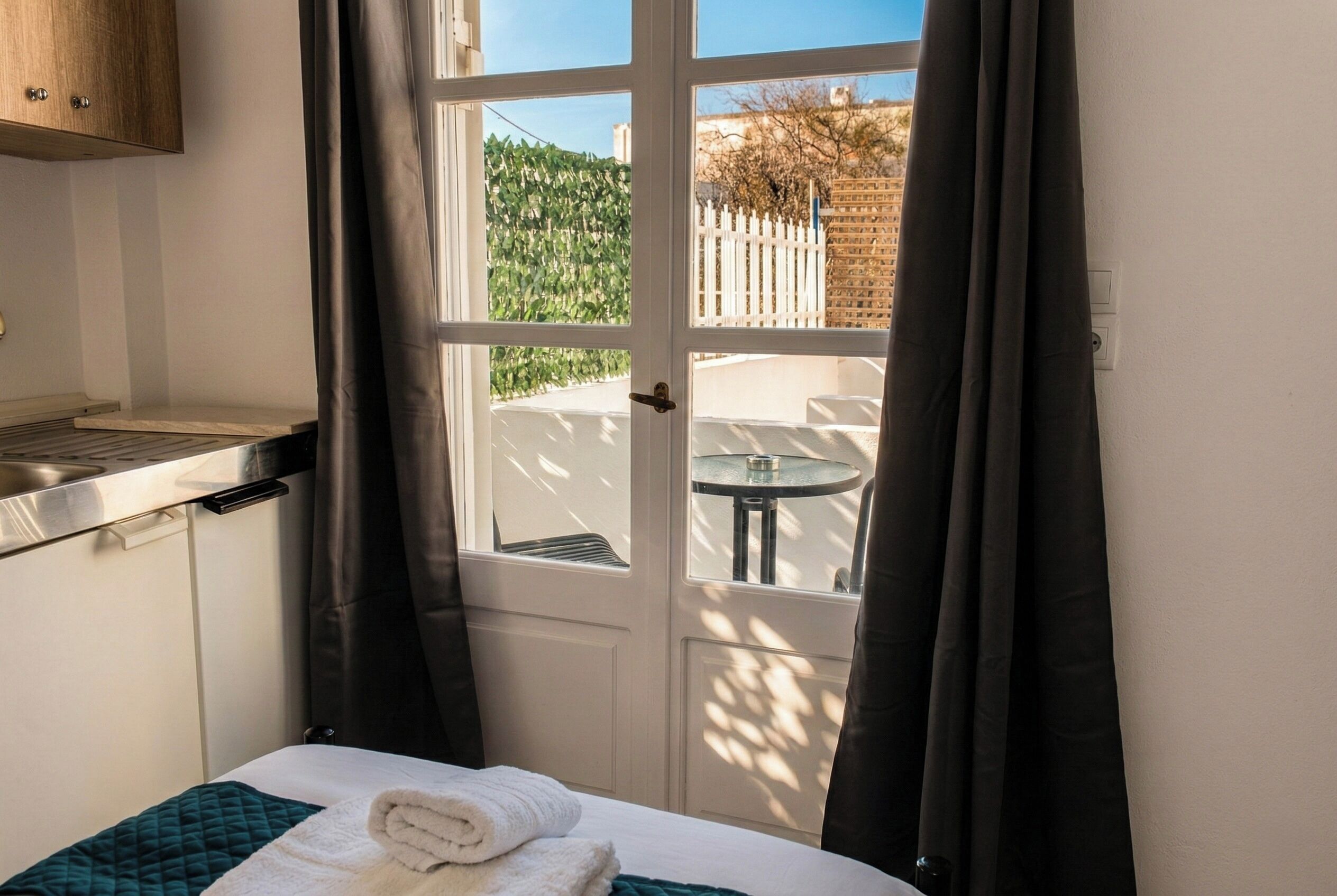 Ein Hotelzimmer mit Bett, kleinem Tisch, einem Fenster mit Vorhängen und Blick ins Freie.