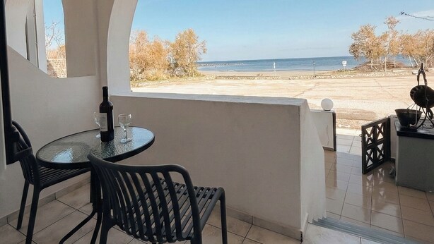 Een overdekt terras buiten met een tafel en stoelen, een fles wijn, en uitzicht op het strand en de oceaan.