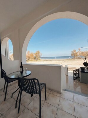 Een overdekt terras buiten met een tafel en stoelen, een fles wijn, en uitzicht op het strand en de oceaan.