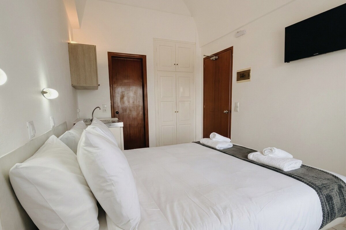 A hotel room with a bed, a wooden door, a white wall, and a flat-screen TV.