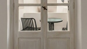 Een witte deur met glaspanelen, een zwarte stoel en een kleine ronde tafel zijn zichtbaar door de deur.