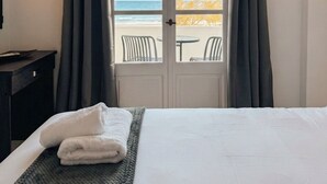 Hotelkamer met een bed, bureau, airconditioning en uitzicht op het strand door een deur.