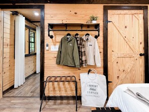A wooden interior with a rack of clothing, a laundry service bag, and a bed. - RRG Cabin l Treetop Deck•HotTub•Firepit•Putting•OutdoorTV•Sleeps8•Pets (Campton)