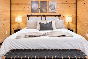 A neatly made bed with a headboard, two bedside lamps, and three wall-mounted artworks. - Cozy Winter Cabin: Steamy Hot Tub, Fire Pit, Game Room, Family + Pet Friendly (Campton)