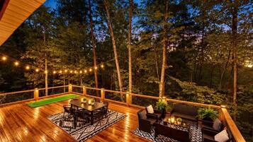 A wooden deck with a pool table, outdoor seating, and string lights.