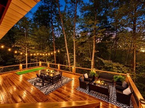 A wooden deck with a pool table, outdoor seating, and string lights. - Cozy Winter Cabin: Steamy Hot Tub, Fire Pit, Game Room, Family + Pet Friendly (Campton)