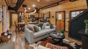 A cozy cabin interior with a dining area, a sofa, and a kitchen. - RRG Cabin l Treetop Deck•HotTub•Firepit•Putting•OutdoorTV•Sleeps8•Pets (Campton)