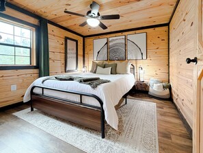 Une chambre à coucher avec un lit, un ventilateur de plafond, une table de chevet avec une lampe et une fenêtre.