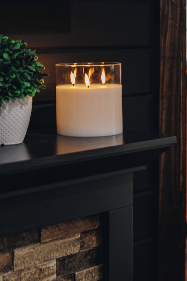 Une bougie blanche dans un porte-bougie en verre, posée sur une étagère en bois sombre.