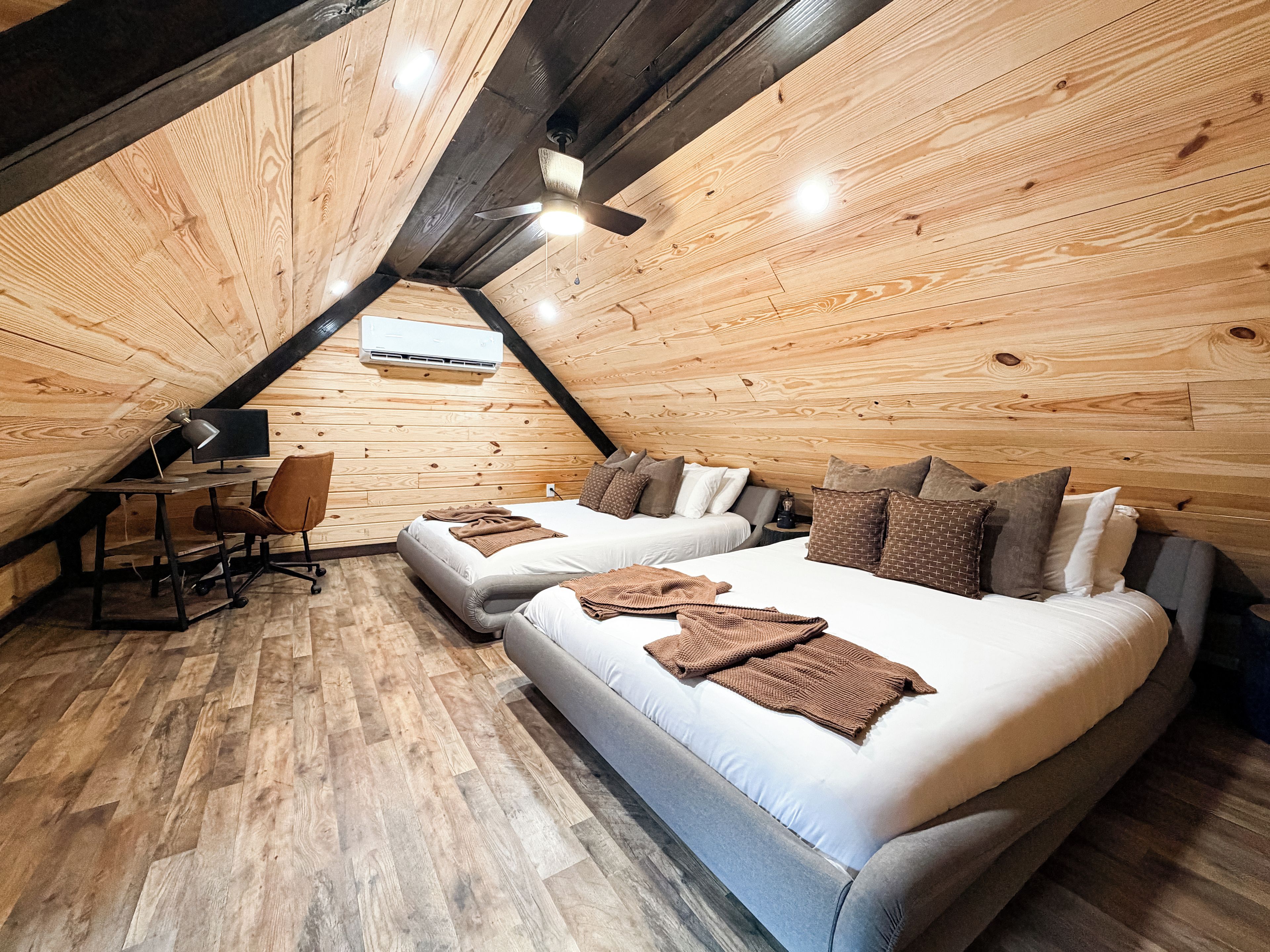 A cozy attic bedroom with a loft bed, a desk with a computer, and a chair.