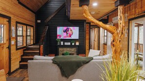 A cozy cabin interior with a wooden staircase, a fireplace, a television, and a sofa. - RRG Cabin l Treetop Deck•HotTub•Firepit•Putting•OutdoorTV•Sleeps8•Pets (Campton)