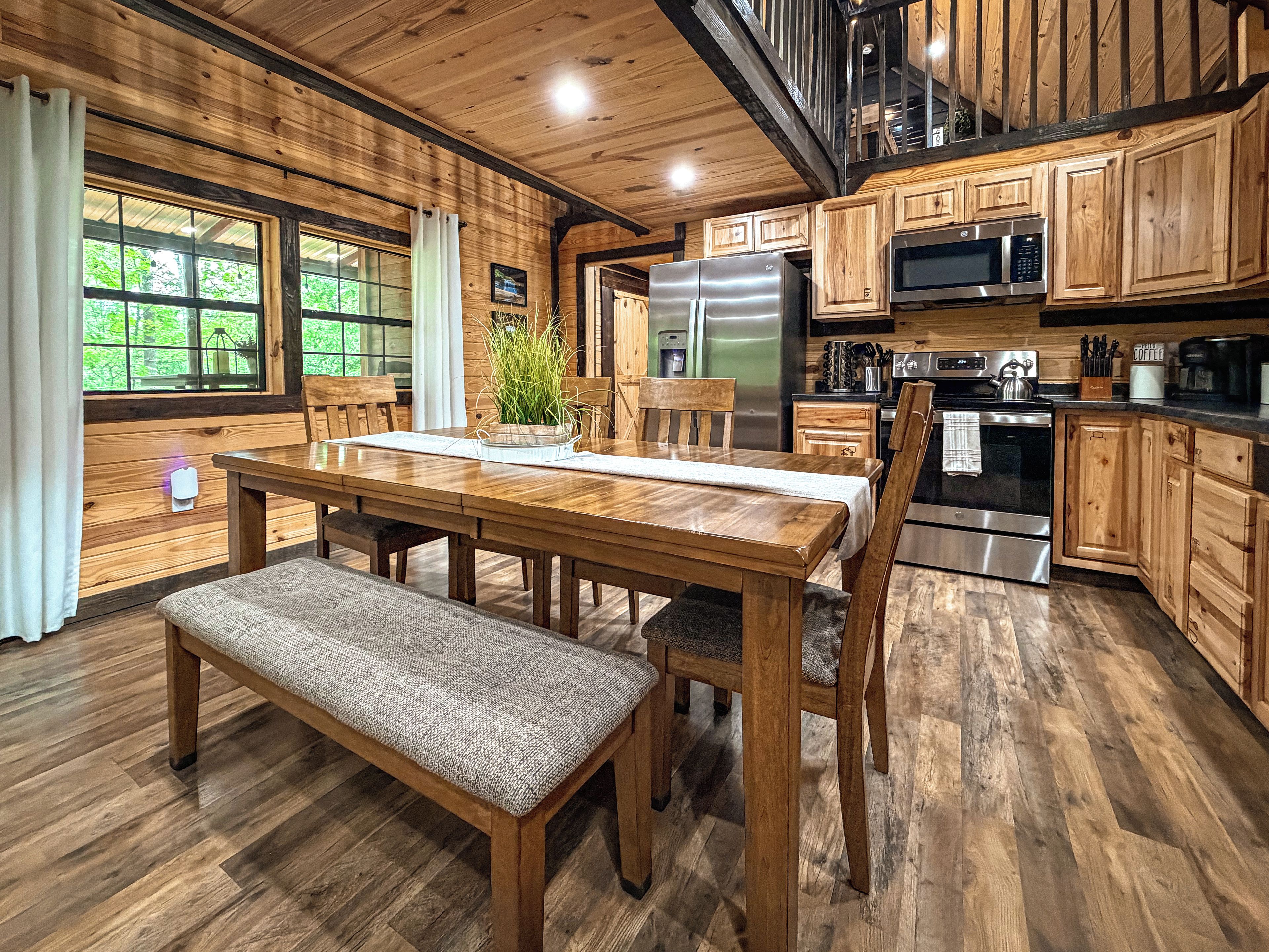 A wooden interior with a dining table, chairs, a bench, a refrigerator, a microwave, and a stove.