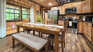 A wooden interior with a dining table, chairs, a bench, a refrigerator, a microwave, and a stove.